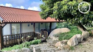 Une maison avec un toit en tuiles, une véranda et un jardin agrémenté de rochers et de plantes.