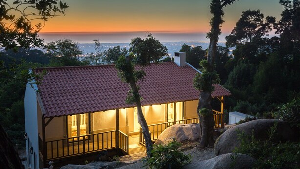 Une maison avec un toit recouvert de tuiles rouges, un balcon et une vue sur la ville au coucher du soleil.