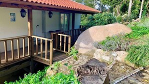 Une maison avec un toit recouvert de tuiles rouges, une terrasse en bois et un mur en pierre.