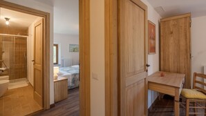 Una habitación con puerta de madera, una mesita con una silla y una cama con ventana.