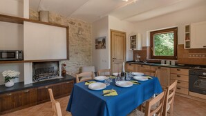 Un comedor con mantel azul, sillas de madera y pared de piedra.