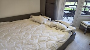 Ein großes Bett mit weißer Bettwäsche, ein dunkles Kopfteil und Blick auf eine Terrasse mit Stühlen und einem Tisch.