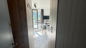 Ein schmaler Flur mit Holzboden führt zu einem Essbereich mit Tisch und Stühlen, an der Wand ist ein Fernseher angebracht.