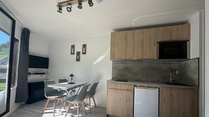 Eine moderne Küche mit Holzausstattung, einer eingebauten Mikrowelle und einem Geschirrspüler. Ein Essbereich mit Tisch und Stühlen lädt zum Verweilen ein, und ein großes Fenster bietet einen Blick ins Freie.