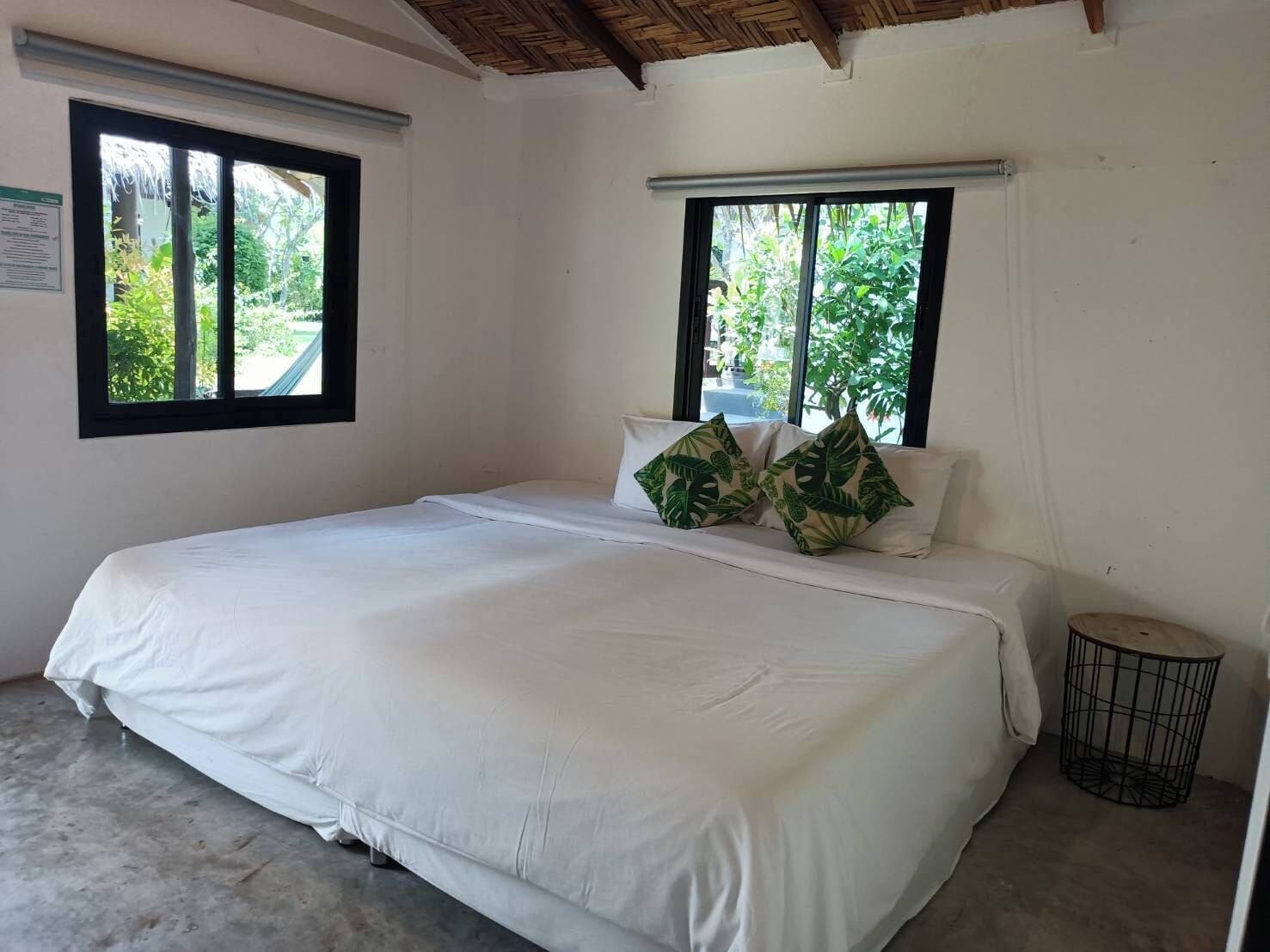 A single bed with white bedding and two windows with black frames.