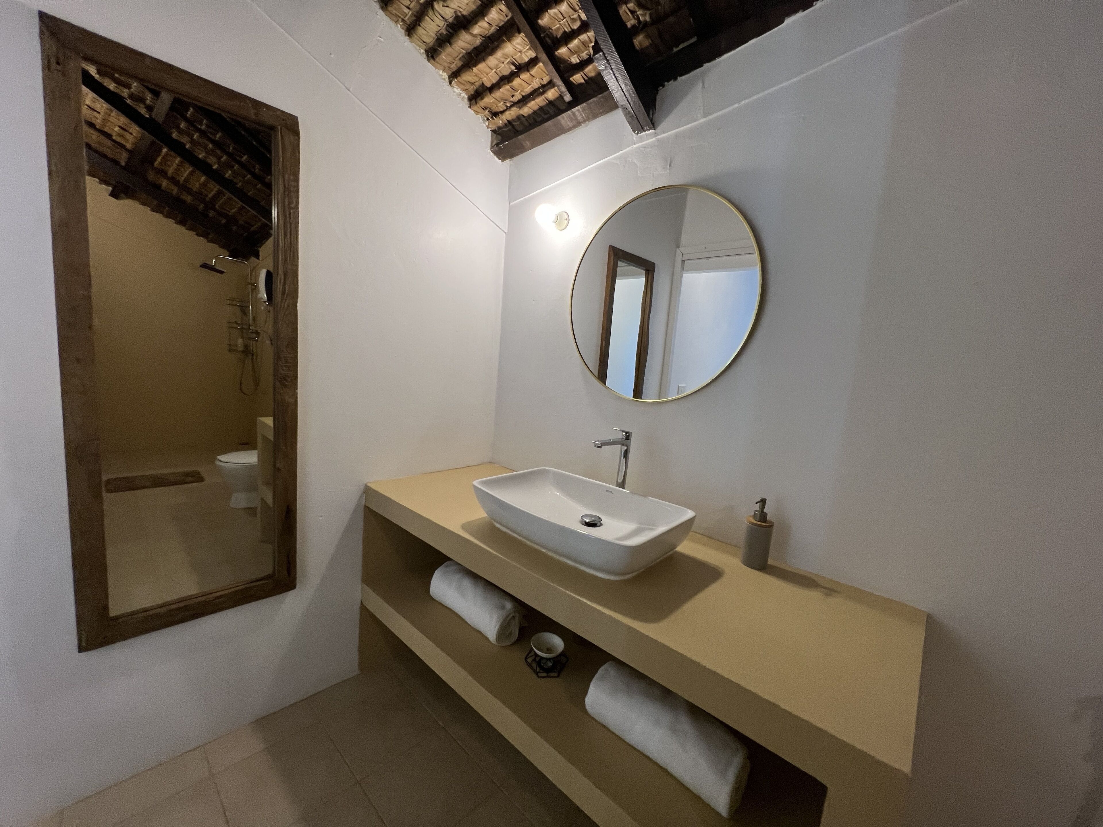 Un baño con un lavabo blanco, un espejo redondo y un perchero para toallas.