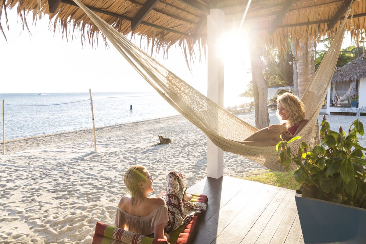 Une scène de plage avec un hamac, une terrasse en bois et une vue sur la mer.
