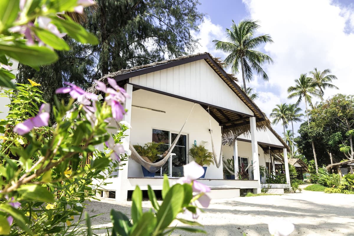 Un bâtiment blanc doté d’un porche, d’un hamac et de plantes en pot.
