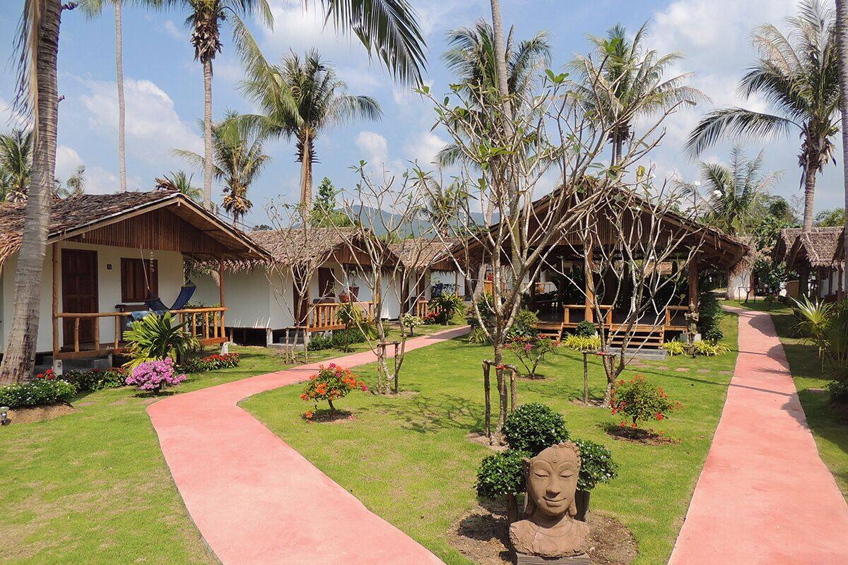 Un complexe hôtelier comprenant plusieurs bâtiments de style bungalow, un chemin principal et une grande variété de plantes et d’arbres tropicaux.