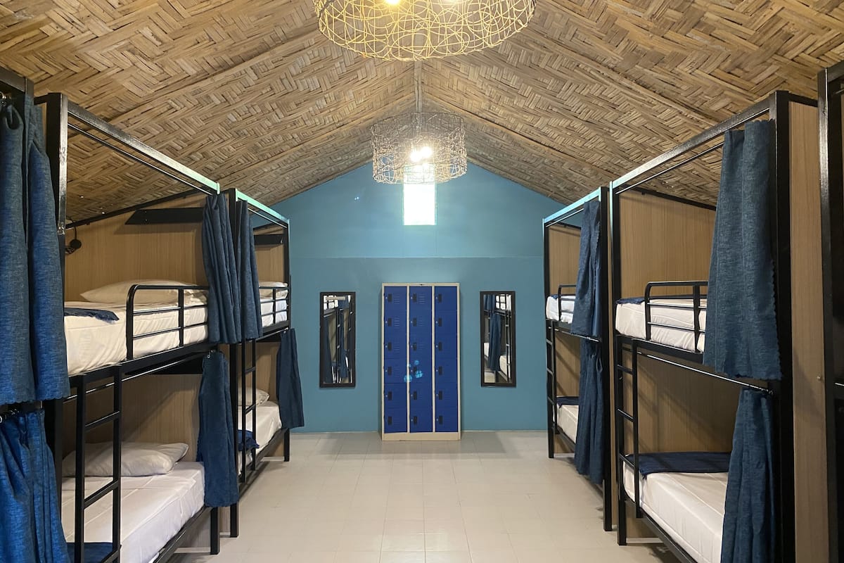 Une chambre de dortoir avec des lits superposés, une porte bleue et un plafond en bois.