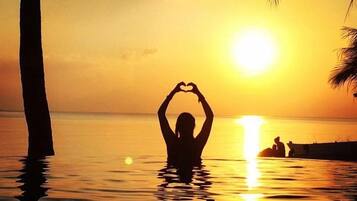A person making a heart shape with their hands in the water at sunset.