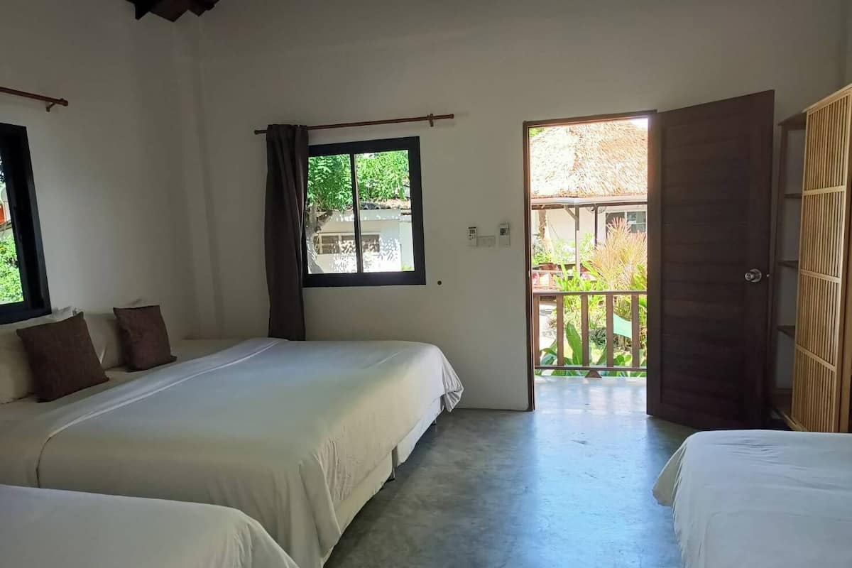 Une chambre avec deux lits, une fenêtre et une porte ouverte donnant sur un espace extérieur.