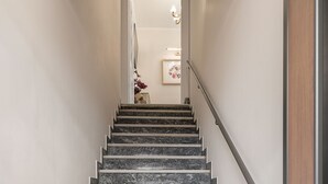 Una escalera con peldaños de mármol y blanco que conduce a una habitación con candelabro e imágenes enmarcadas.