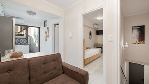 Una sala moderna con un sofá, una mesa de comedor con un encimera de vidrio y vista a un dormitorio con cama y chimenea.