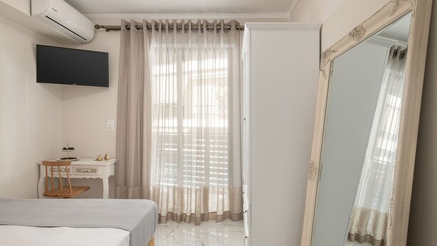 Un dormitorio con cama, escritorio, silla, televisor y un espejo grande.