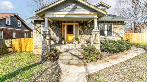 A stone house with a yellow door, a stone porch, and a small garden.