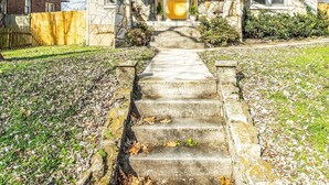 A stone house with a front porch, a stone staircase leading to the entrance, and a fenced yard.