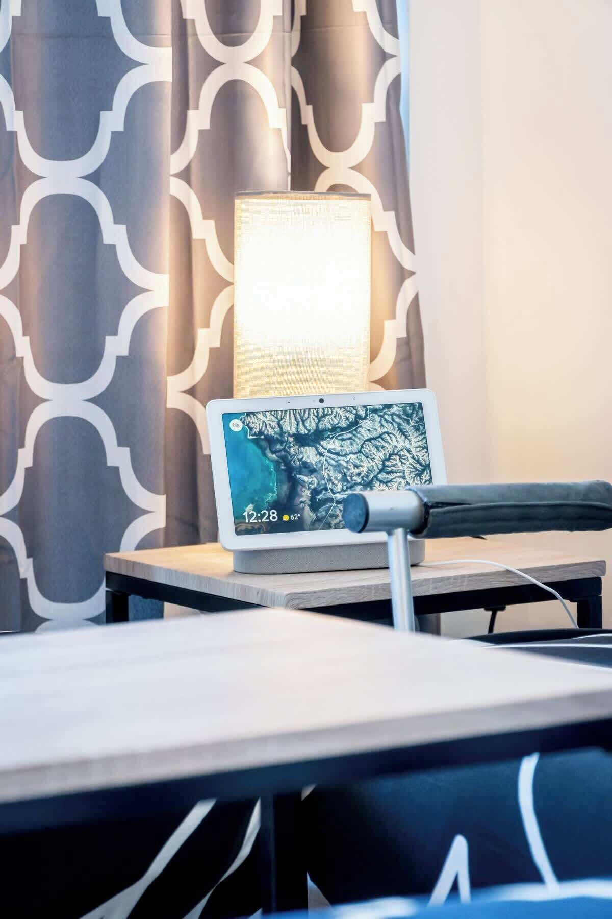 Ein Hotelzimmer mit modernem Design, das einen Schreibtisch mit einem Laptop, eine Lampe und einen gemusterten Vorhang im Hintergrund zeigt.