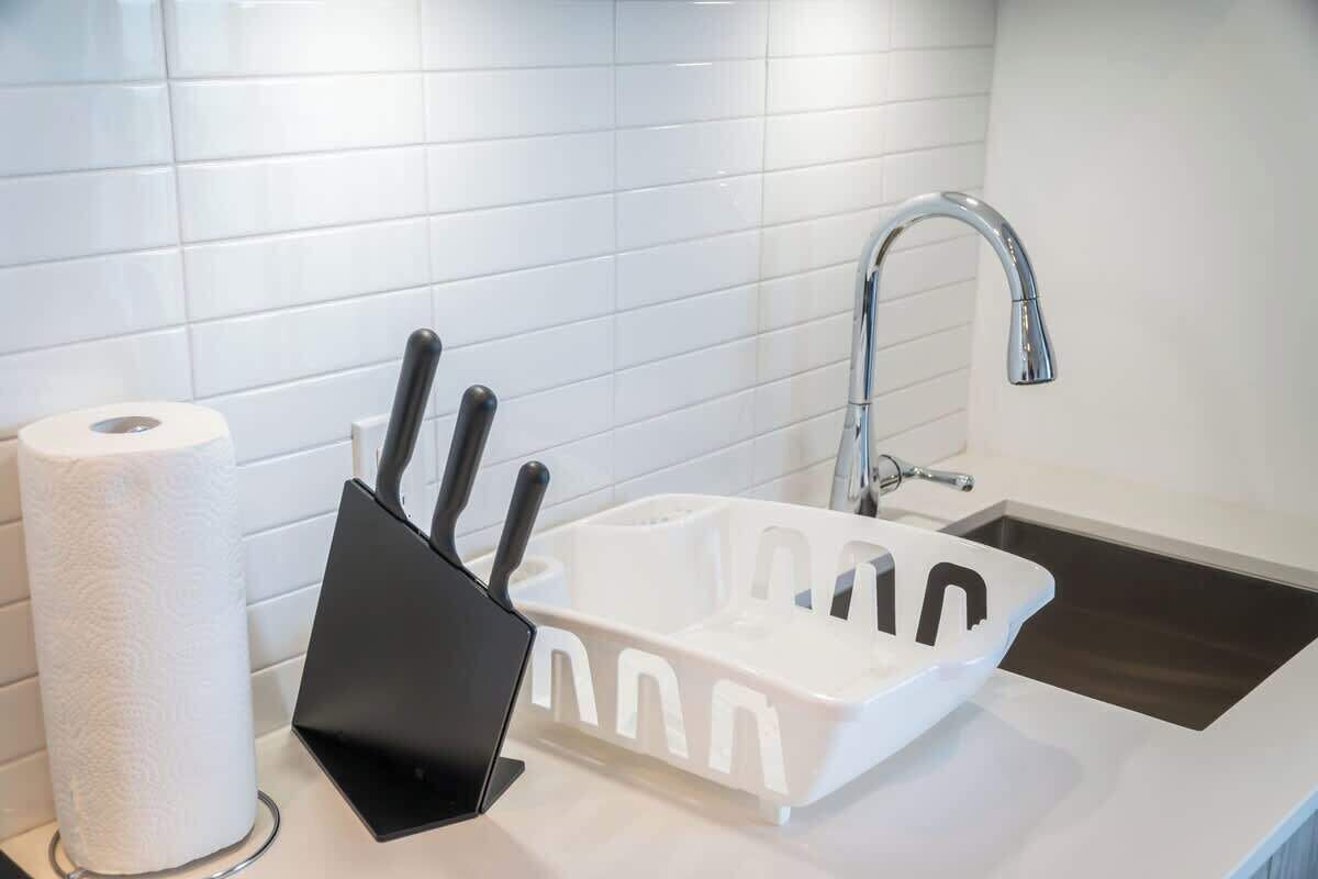 A modern bathroom with a white sink, a black knife block, and a roll of toilet paper.