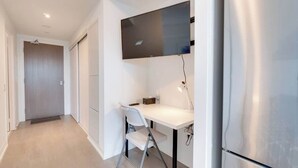 Moderni keittiö, jossa on sisäänrakennettu jääkaappi, seinälle asennettu litteänäyttöinen televisio valkoisen työtason yläpuolella ja kokoontaitettava tuoli.