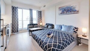 Moderni hotellihuone, jossa on suuri sänky, työpöytä ja suuret ikkunat, joista avautuu näkymä kaupunkiin.