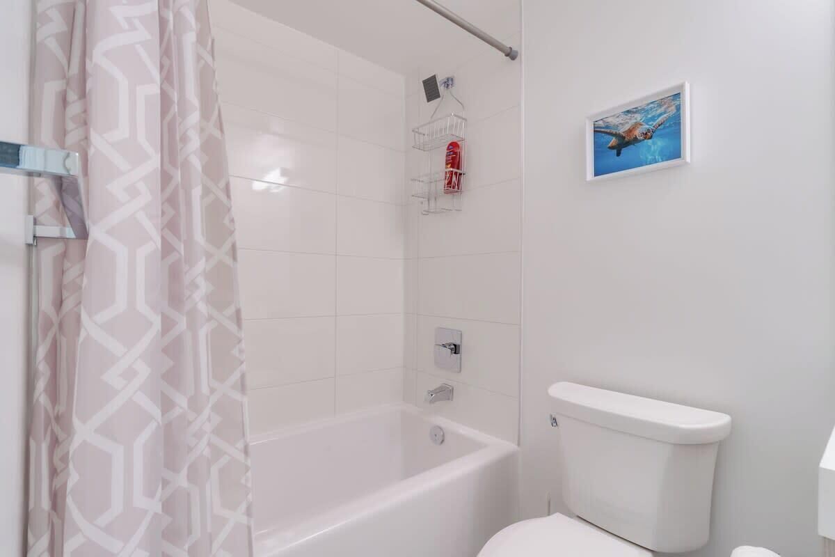A bathroom with a bathtub, toilet, shower curtain, and a framed picture on the wall.
