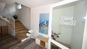 Un interior moderno con una escalera, una silla blanca, una consola de madera y un cuadro de un paisaje urbano.