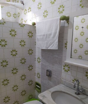 Ein Badezimmer mit Waschbecken, Spiegel und Fliesen in Grün-Weiß-Muster.