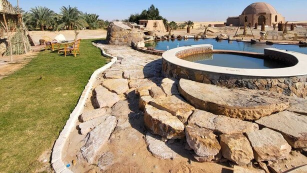Zona de piscina con estructuras de piedra y un edificio en forma de cúpula al fondo.