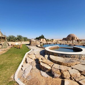 A pool area with stone structures and a dome-shaped building in the background. - Qasr El Bagawat Eco Lodge Hotel (El Kharga)