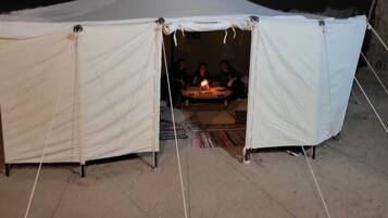 A white tent with a table inside, where three people are seated around a lit candle.