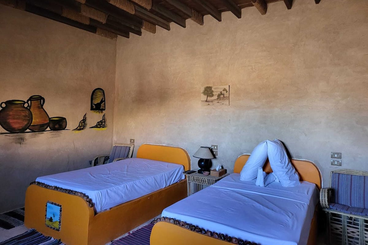 Une chambre avec deux lits, une petite table et un mur décoré.