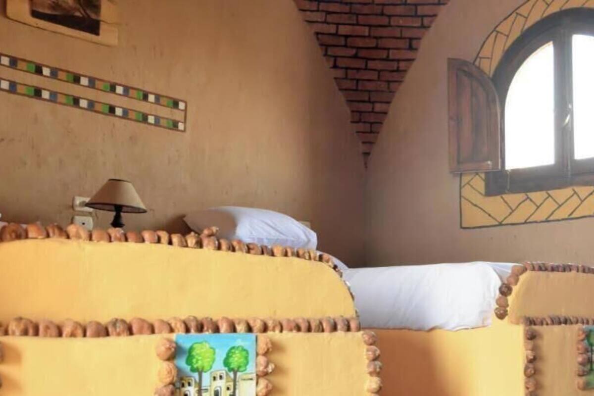 Une pièce comprenant un lit, une lampe, une fenêtre et un mur orné d’un motif géométrique.
