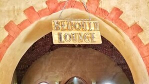 Una zona de estar acogedora con un letrero que dice "BIRHULL LOUNGE" bajo un arco de ladrillo. Hay bancos y una mesa con una estatua en el centro.