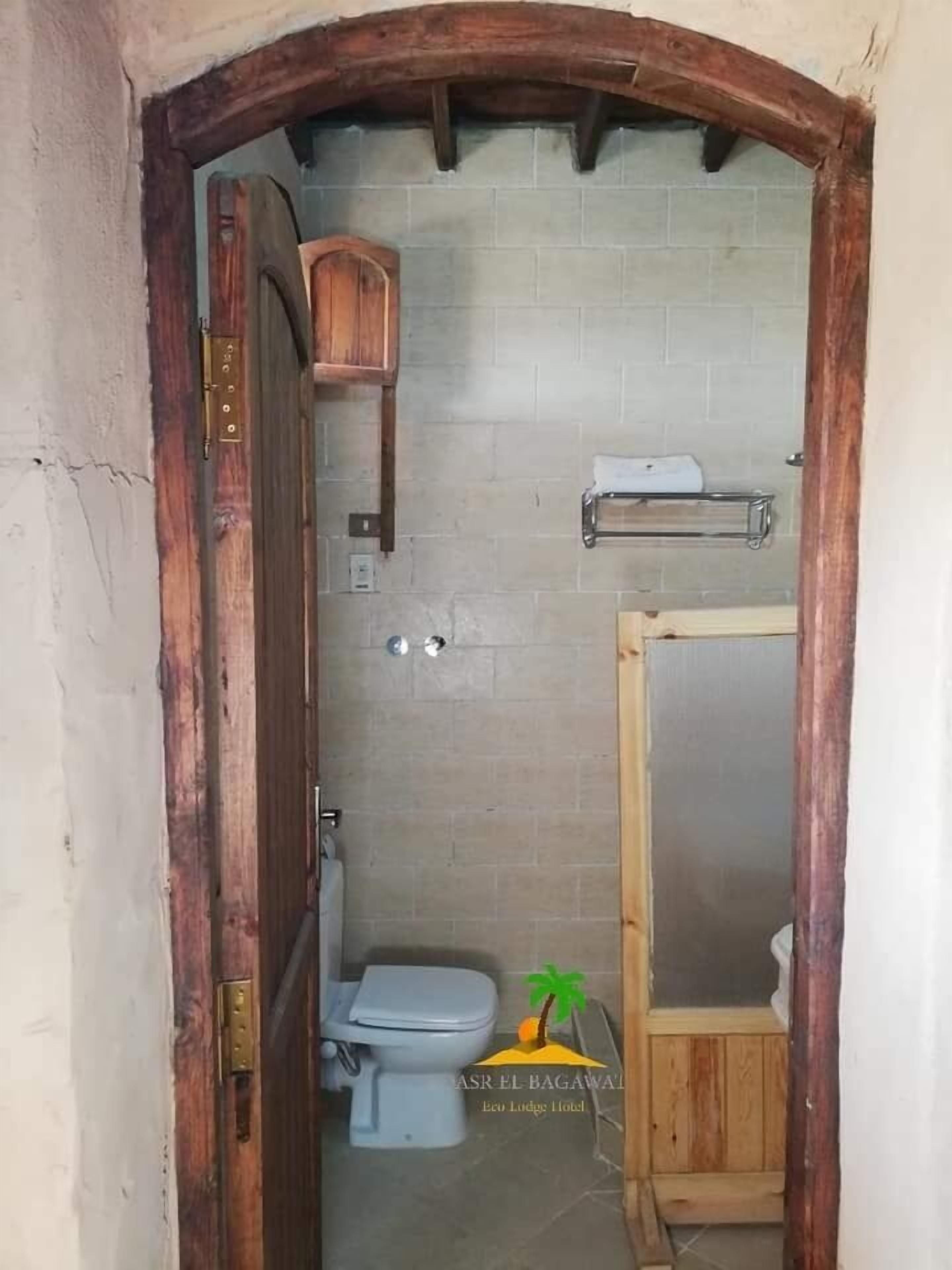A bathroom with a toilet, a wooden shelf, and a shower area.