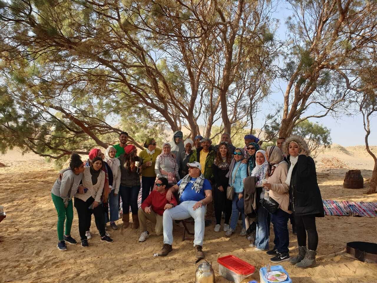 Eine Gruppe von Menschen versammelt sich unter einem Baum in einer Wüstenlandschaft.