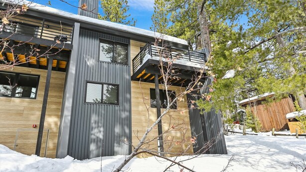 Una casa moderna de dues plantes amb un balcó, envoltada d'arbres i coberta de neu.