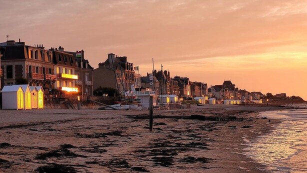 Een kustplaats met gebouwen langs de oever, een zandstrand en een ondergaande zon.