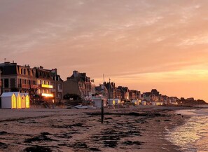 A beachside town with buildings along the shore, a sandy beach, and a sunset.