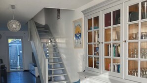Een ruime woonruimte met een trap, een witte kast met glazen deuren, en een blauwe stoel.