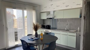 Een moderne keuken met een eethoek, met een ronde tafel, twee stoelen, een vaas met gedroogde planten en een fles sinaasappelsap.