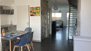 Een moderne keuken met een eethoek, een kleurrijk fruit schilderij en een trap naar een hoger niveau.