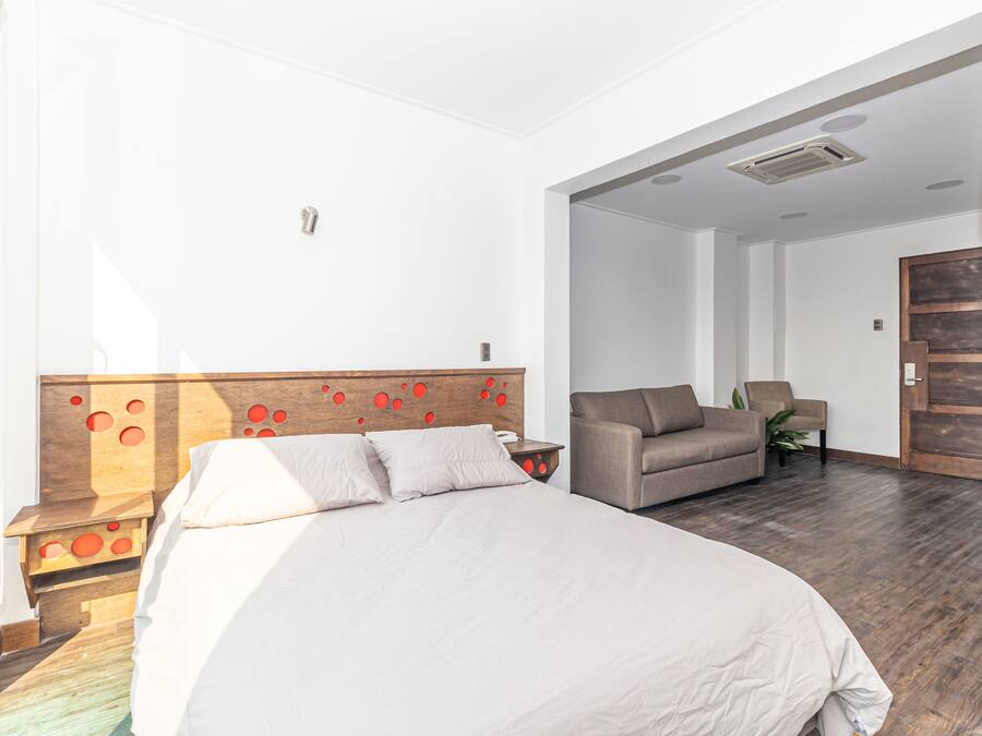 Een hotelkamer met een groot bed, een slaapbank en een houten hoofdbord met rode accenten.