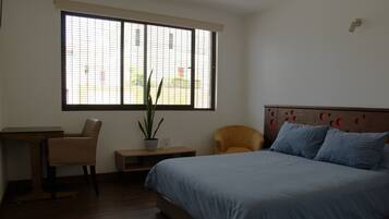 A bedroom with a bed, a desk, a chair, and a potted plant.