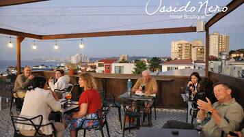 A rooftop terrace with people dining, a view of the city, and the text "Ossido Nero Hotel Boutique".