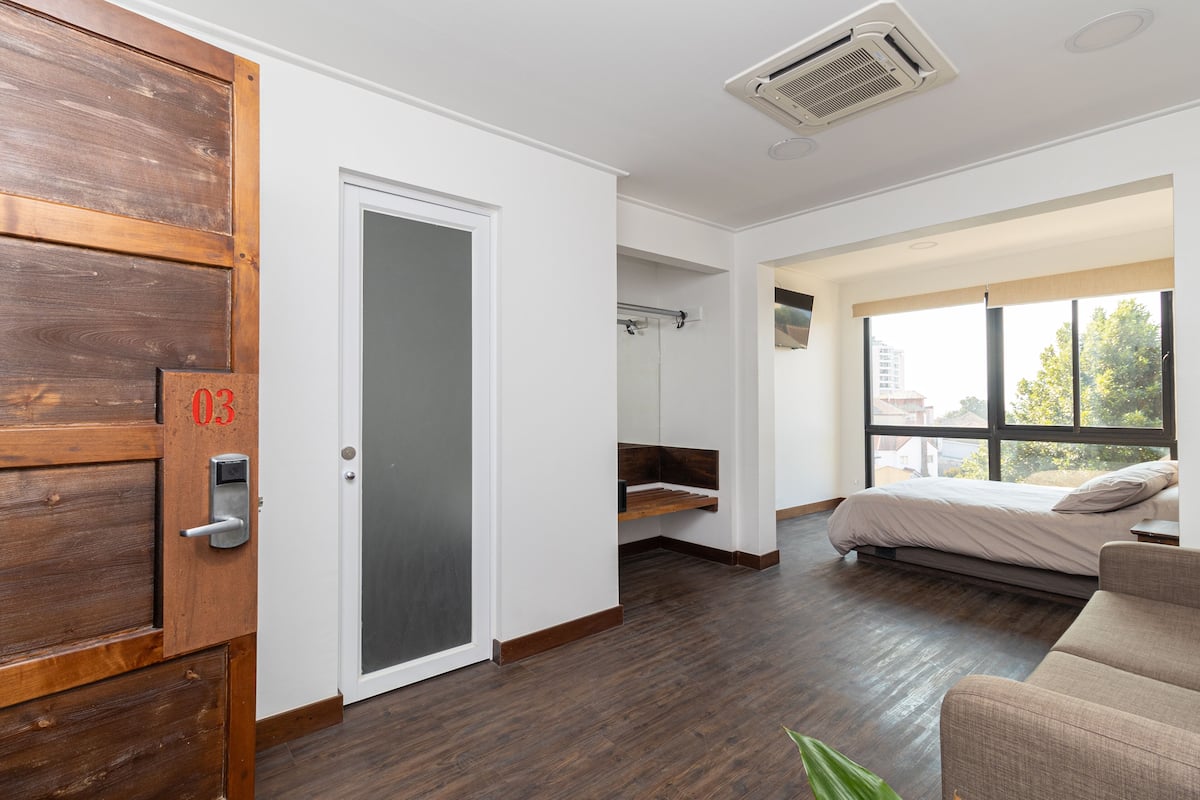 Una stanza moderna con una porta in legno, un letto con testiera, una finestra vista e uno scaffale a incasso.