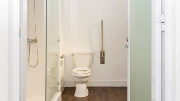 Un baño pequeño con suelo de madera, un inodoro y una zona de ducha.