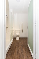 Un baño pequeño con suelo de madera, un inodoro y una zona de ducha.