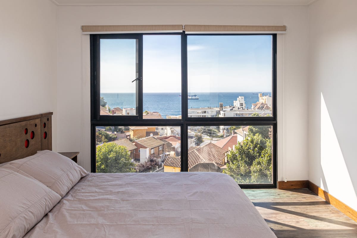 Una camera da letto con un'ampia finestra che si affaccia sul mare e sugli edifici.