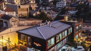 Un edificio moderno con un letrero de neón, zona de estacionamiento y edificios residenciales aledaños.